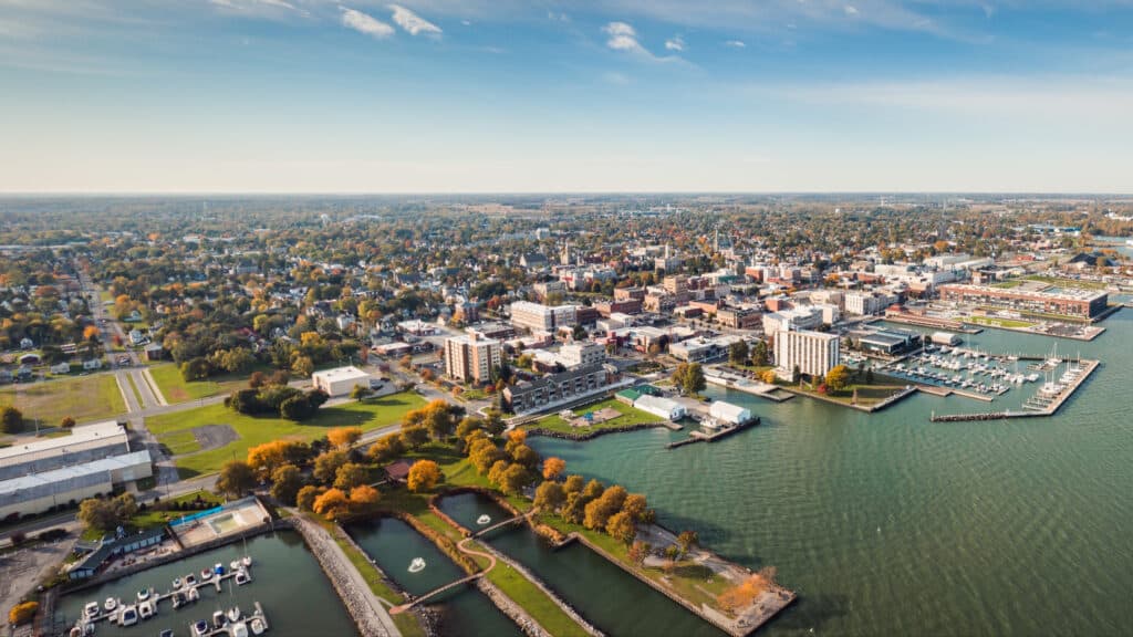 Incredible aerial city skyline panorama photograph of Sandusky, Ohio from the shoreline of the bay in Lake Erie with parks and harbors seen below on a sunny day.